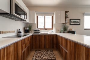 Modern kitchen with wooden cabinets and white countertops, bright natural light from window.