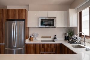 Modern kitchen with stainless steel refrigerator and microwave, white cabinets, and natural light fr.