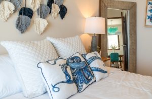 Bright bedroom with nautical-themed pillows and cozy decor, perfect for relaxing in a seaside home.