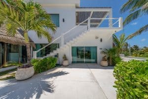 Modern beachfront villa with white exterior, outdoor staircase, lush tropical plants, and clear blue. Isla Mujeres Mexico Property