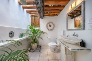 Rustic bathroom with wooden ceiling beams, white walls, and natural decor in a tropical property. Isla Mujeres Mexico Property