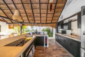 Modern kitchen with thatched roof, black cabinetry, and tropical outdoor views at Mundaca Real Estat. Isla Mujeres Mexico Property