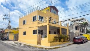 Modern yellow residential building in a tropical neighborhood, featuring multiple floors and rooftop. Isla Mujeres Mexico Property