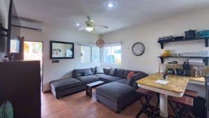 Bright living room with gray sectional sofa, wall clock, and open kitchen area in a modern home. Isla Mujeres Mexico Property