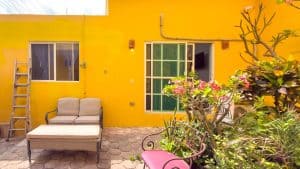 A colorful yellow exterior wall of a house with a patio, featuring a beige outdoor sofa, a ladder, a. Isla Mujeres Mexico Property