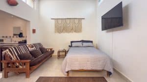 Modern bedroom with a bed, sofa, wall-mounted TV, and minimal decor in a residential property. Isla Mujeres Mexico Property