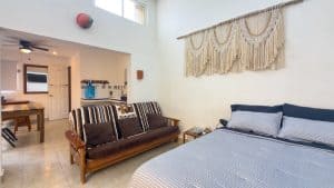 Modern bedroom with a cozy bed, vintage sofa, and decorative wall hanging in a bright, airy space. Isla Mujeres Mexico Property