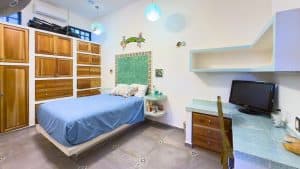 A comfortable bedroom with wooden storage, a blue bed, and a workspace with a computer. Isla Mujeres Mexico Property