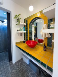 Bright bathroom with yellow and green tiled countertop and red vessel sink, modern decor, and a larg. Isla Mujeres Mexico Property